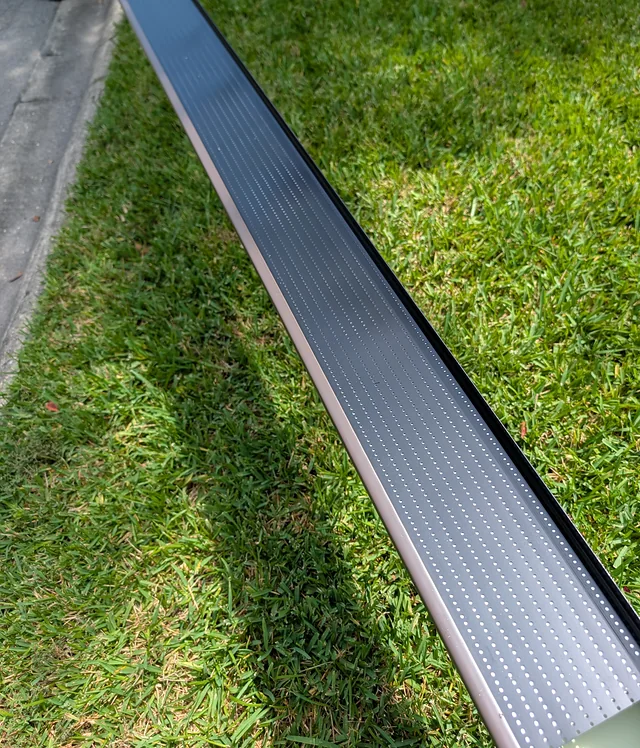 Long gutter section with perforated guards being prepared beside a lawn.